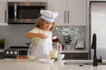 Kid chef cook in chef hat preparing food on kitchen. Child making tasty delicious. Cooking meal.