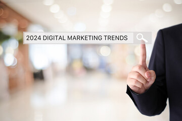 Businessman hand touching 2024 digital marketing trends search bar over blur office background, banner, SEO 2024 business trends planning, success in business concept
