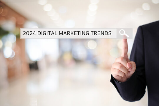 Businessman hand touching 2024 digital marketing trends search bar over blur office background, banner, SEO 2024 business trends planning, success in business concept