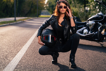Sexy biker girl, kneeling on tarmac in front of motorcycle, looking at camera 