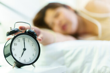 Asian oversize fat woman sleep on the bed in morning, during the time, an alarm clock is alarming and woman trying to snooze an alarm clock. Lazy woman wake up late in the morning.
