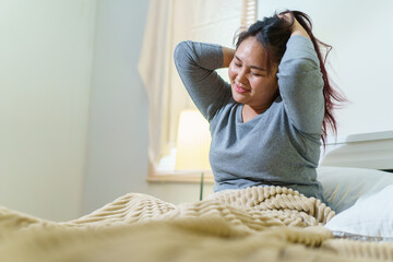 Asian oversize fat woman sitting on the bed in morning after woke up from the bed and making a...