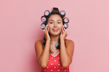 Obraz na płótnie Canvas Young cheerful Asian woman doing her face using eye patches, twisting her hair on curlers, getting ready for work, good morning concept, copy space