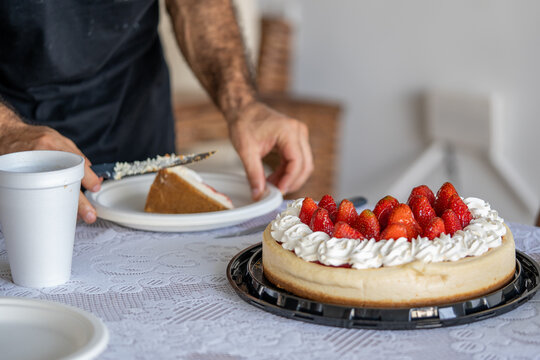 hombre mexicano cortando trozo de tarta de fresas con crema chantilly en platos desechables