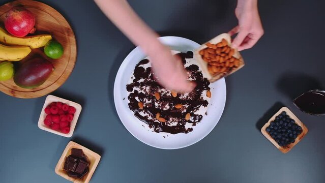 A woman decorates a stracciatella cake with almonds. Top view of kitchen table. Cooking in the kitchen.