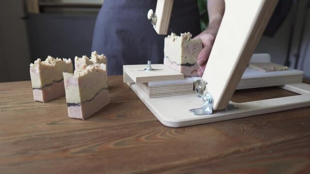 A woman master soap maker cuts handmade soap on a wooden string cutter. Home production of natural cosmetics