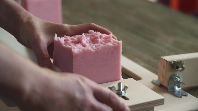 A woman master soap maker cuts handmade lavender soap on a wooden string cutter. Home production of natural cosmetics