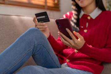 Happy young Asian woman using smartphone and credit card for online shopping on sofa at home.