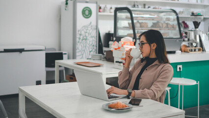 Asian business woman working on a laptop while enjoying a cup of coffee in a cafe
