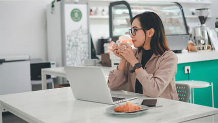 Asian business woman working on a laptop while enjoying a cup of coffee in a cafe
