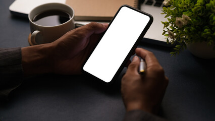Close up view of man using smartphone at working desk. Blank screen mobile phone for your text or graphic display montage.