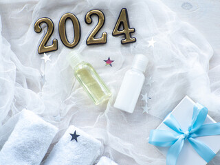 Fototapeta na wymiar Christmas composition with 2024, towels, giftbox and body care products in bottles. New year Wellness card. Christmas, body and skincare concept. Hygiene and spa, relaxation as a gift for holidays.