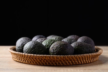 Ripe hass avocado fruit in basket on wooden table with black background