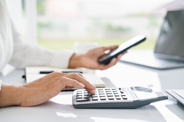 hands of business woman, female entrepreneur using calculator and mobile phone during online working on laptop computer on office table at home, telecommuting, work from home concept