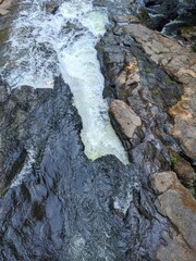 Top down view of stream flowing around boulders in a rocky river bed, at the edge of a waterfall. 