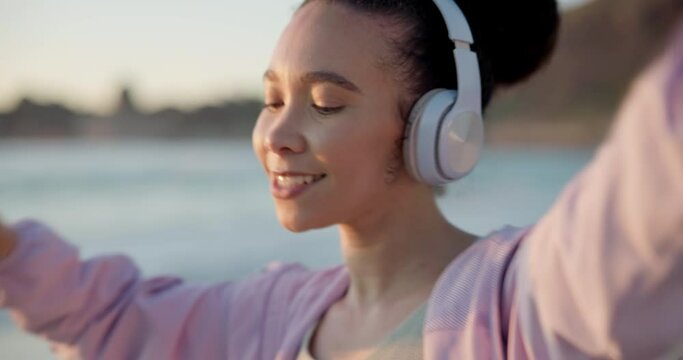 Dance, headphones and woman with music at the beach for outdoor cardio workout or training. Happy, energy and female person moving and listening to song, playlist or radio by the ocean for exercise.