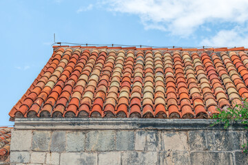 Building with red tiled roof in the Old Town of Budva, Montenegro. Ancient stone facade against a blue sky, close-up