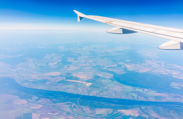Obraz premium Aerial view from airplane window above green ground. View from the airplane window with beautiful clouds at sunrise