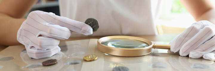 Numismatist in white gloves examines ancient coins collection at table.