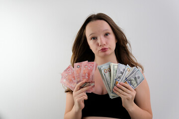 choice between Canadian dollars and US dollars girl weighs in hands a pack of five banknotes of Canadian dollars with large pack of 100 dollar bills twisting lips chooses a lot of money. trip gift