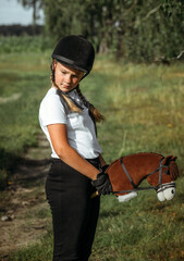 Obraz premium Portrait of a jockey girl in a helmet and a white t-shirt, who sits on a brown toy horse.