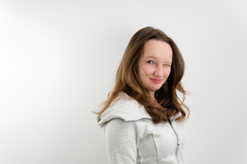 Fototapeta premium young teenage girl turns to camera smiles and blinks first with right and then with left eye light smile playfulness joke good mood. in studio hair developing chic hairstyle well-groomed beauty