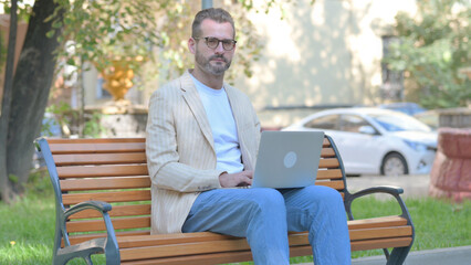 Obraz premium Modern Casual Man Looking at Camera while Working on Laptop Outdoor