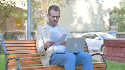 Fototapeta premium Modern Casual Man Talking on Phone and Using Laptop Outdoor