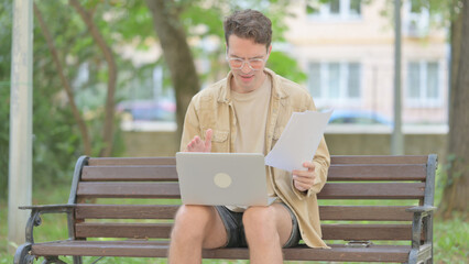 Casual Young Man Feeling Upset while Reading Contract and Using Laptop Outdoor