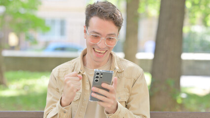 Casual Young Man Celebrating Win on Smartphone Outdoor