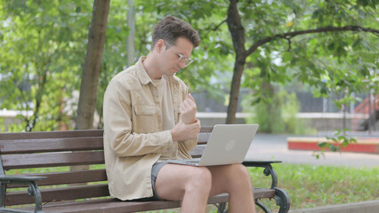 Fototapeta premium Modern Young Man with Wrist Pain Using Laptop Outdoor