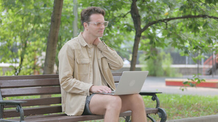 Fototapeta premium Modern Young Man with Neck Pain Using Laptop Outdoor