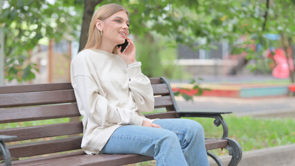 Fototapeta premium Young Woman Talking on phone while Sitting Outdoor on a Bench