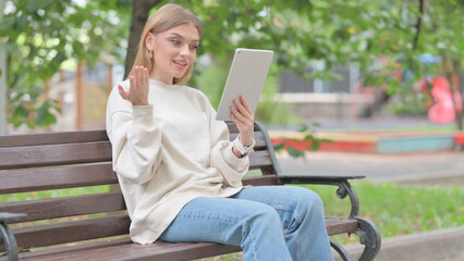 Fototapeta premium Young Woman Doing Video Chat on Tablet while Sitting Outdoor on a Bench