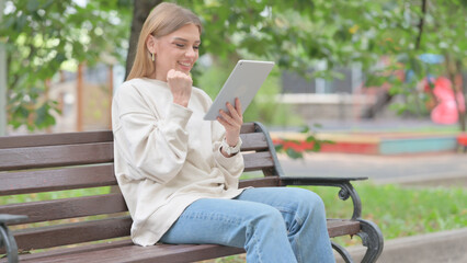 Fototapeta premium Young Woman Celebrating on Tablet while Sitting Outdoor on a Bench
