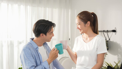 Asian young family couple boy and girl smile with cheers a mug of coffee and hot chocolate milk before drink and sitting on kitchen counter with sunlight window breakfast lifestyle activity