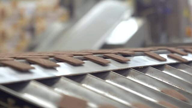 static slow motion close up shot of square, brown, chocolate cookies sliding from a conveyor line on a metal surface