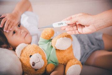 Sick kid. Mother checking temperature of her sick daughter with thermometer in mouth, child laying...