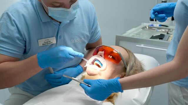 male doctor treats female patient in her cabinet. Close up shot of young woman with an expander in mouth in dental office. Dentist Using Tools, Vacuum, Drill, Equipment, Instruments in clinic