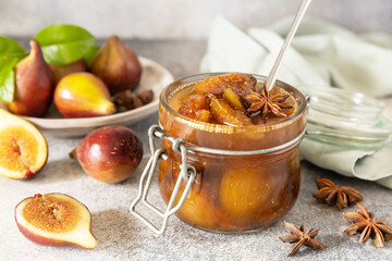 Homemade fig sweet jam in a glass jar with fresh figs on a light gray table. Autumn harvest preservation, healthy fermented food.