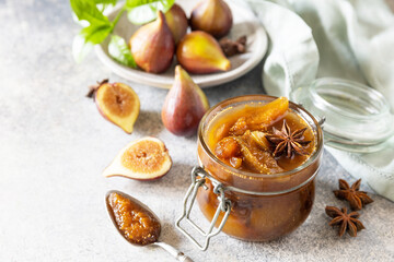 Homemade fig sweet jam in a glass jar with fresh figs on a light gray table. Autumn harvest preservation, healthy fermented food. Copy space.