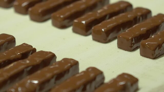 static slow motion medium shot of chocolate bars, freshly made, coated with liquid chocolate on a conveyor line