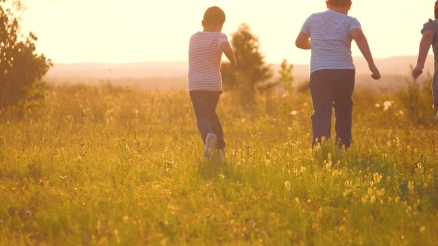Happy little children run together in field lit by sunset light on vacation