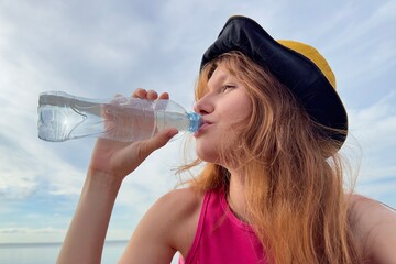 Portrait of young beautiful woman drinking mineral water from plastic bottle at summer day 