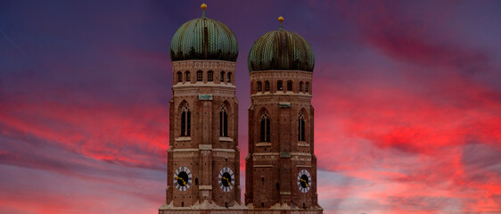 Die zwei Türme der Frauenkirche in der Altstadt von München vor dramatischem, buntem Abendhimmel mit leichter bis mittlerer Bewölkung