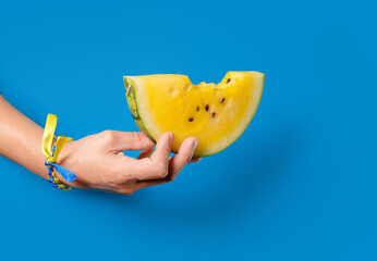 Hand holds a slice of yellow watermelon, as a symbol of Kherson watermelons. The concept of victory and liberation of the Kherson region in Ukraine