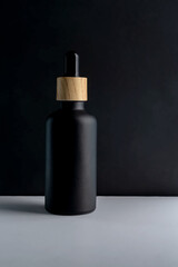 Dark frosted glass cosmetic bottle with a dropper on a black background. Natural cosmetics concept, natural essential oil and skin care products, mockup