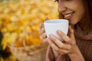 Close up lips of woman drinking hot coffee, holding white cup in hands at autumn park