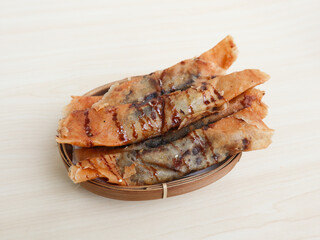 Piscok or banana chocolate is traditional snacks from Indonesia. made of fried banana wrapped in spring roll skin. served on wicker bamboo plate isolated on wooden background