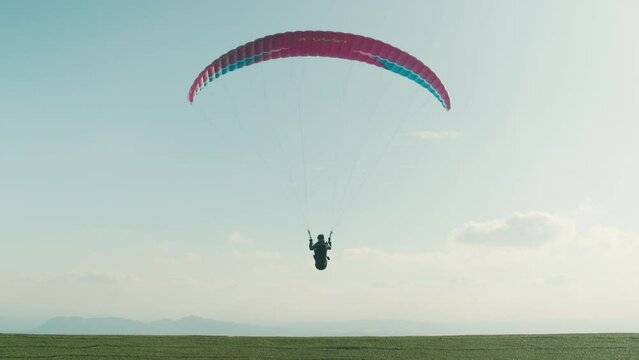 Professional paraglider run and take off from edge of mountain into blue sky. Slow motion shot of man use paragliding parachute to fly